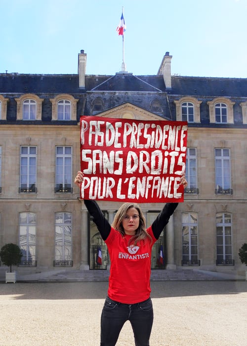 Une militante du collectif Enfantiste devant l'Élysée, pancarte « Pas de présidence sans droits pour l'enfance ».