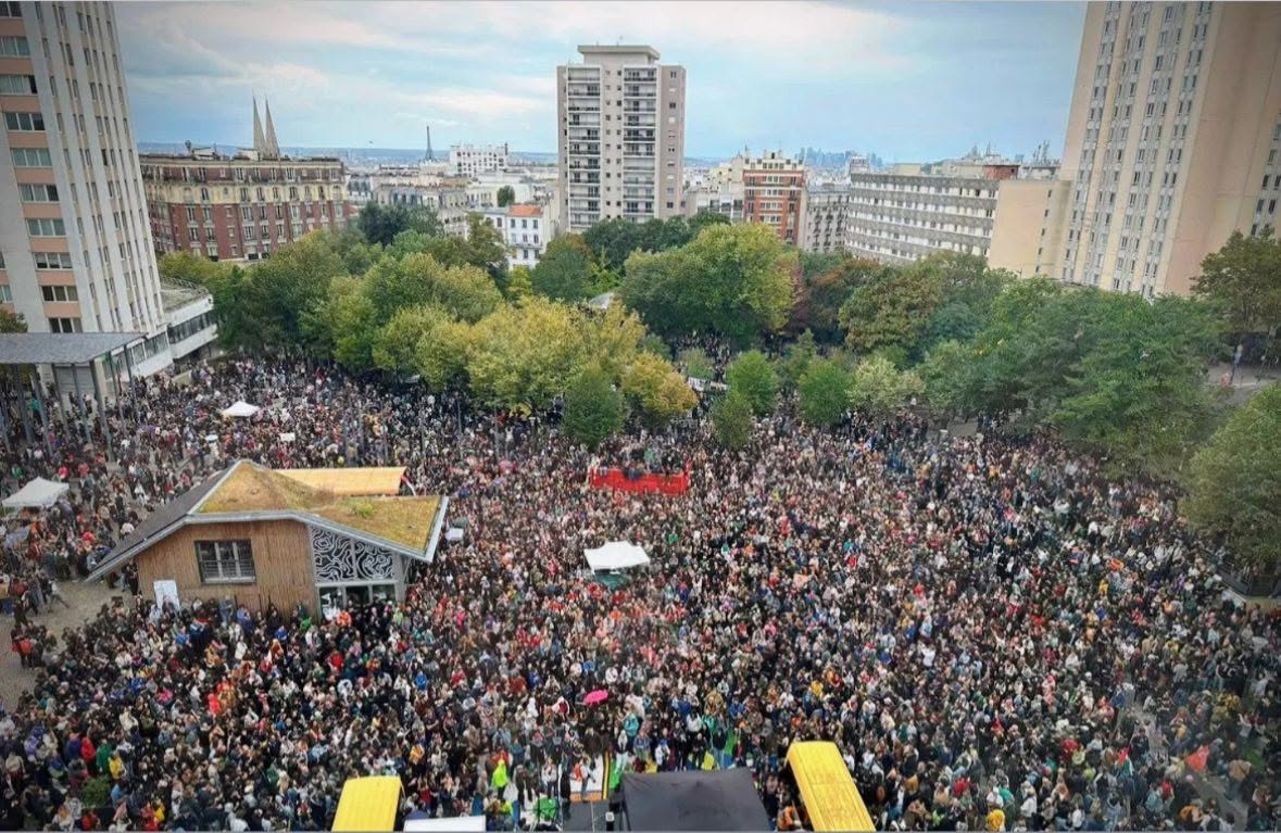 Vue plongeante sur la place des Fêtes, à Paris, noire de monde : une foule immense entre les arbres et les tours d'habitation, avec au loin les toits de Paris et la tour Eiffel.