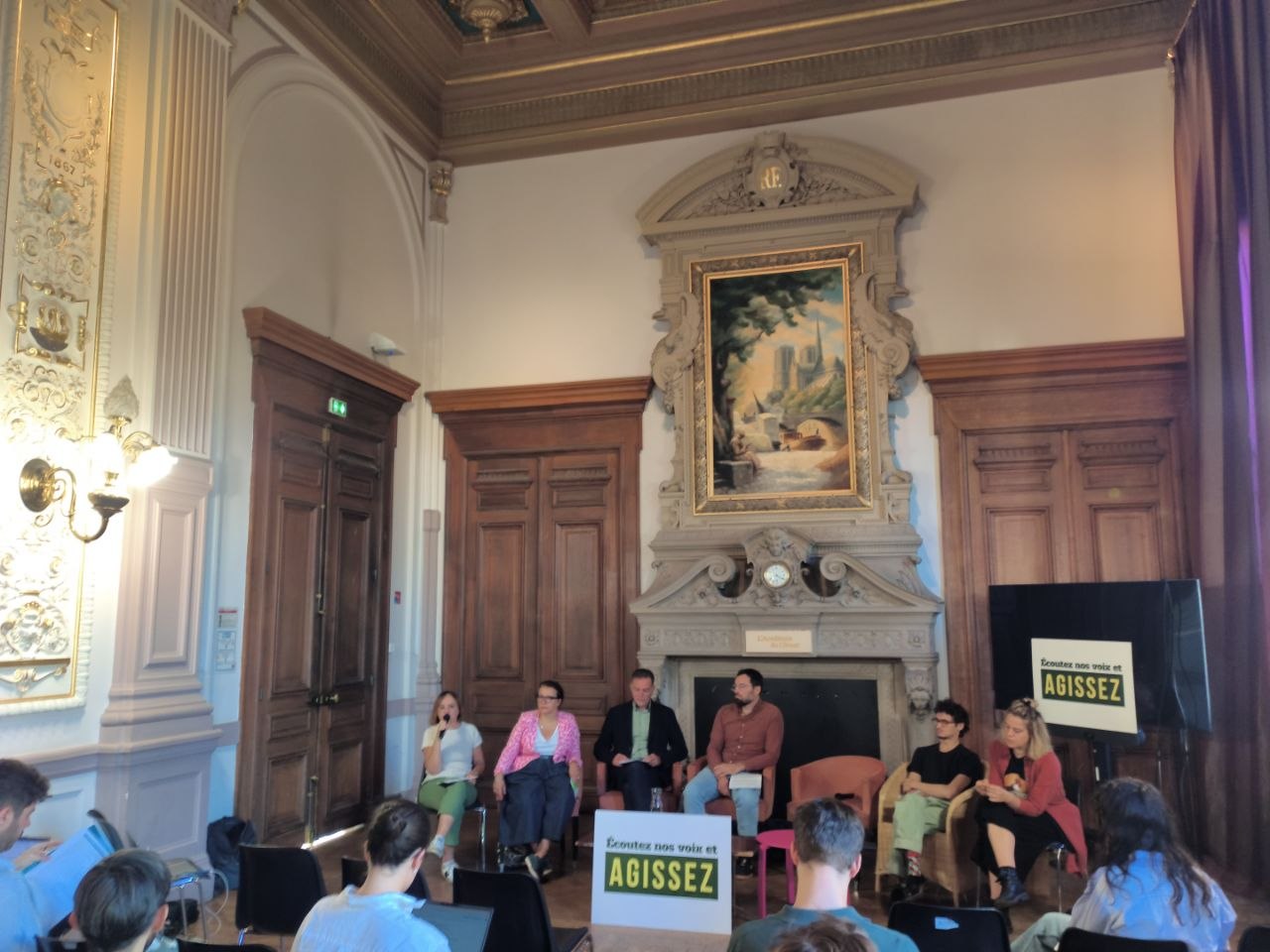 Conférence de presse dans un salon aux boiseries et aux dorures de l'Académie du Climat, à Paris : sept intervenantes et intervenants assis en arc de cercle devant une cheminée monumentale surmontée d'un tableau de Notre-Dame. Une intervenante parle au micro. Au premier plan, des journalistes de dos ; de part et d'autre, deux panneaux « Écoutez nos voix et AGISSEZ ».